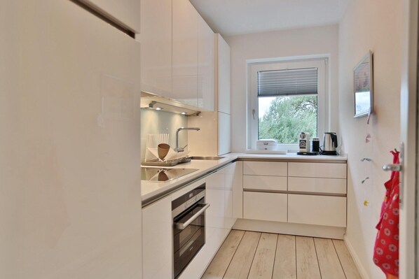 A compact kitchen with white cabinets, a window, and a red towel hanging on the door.