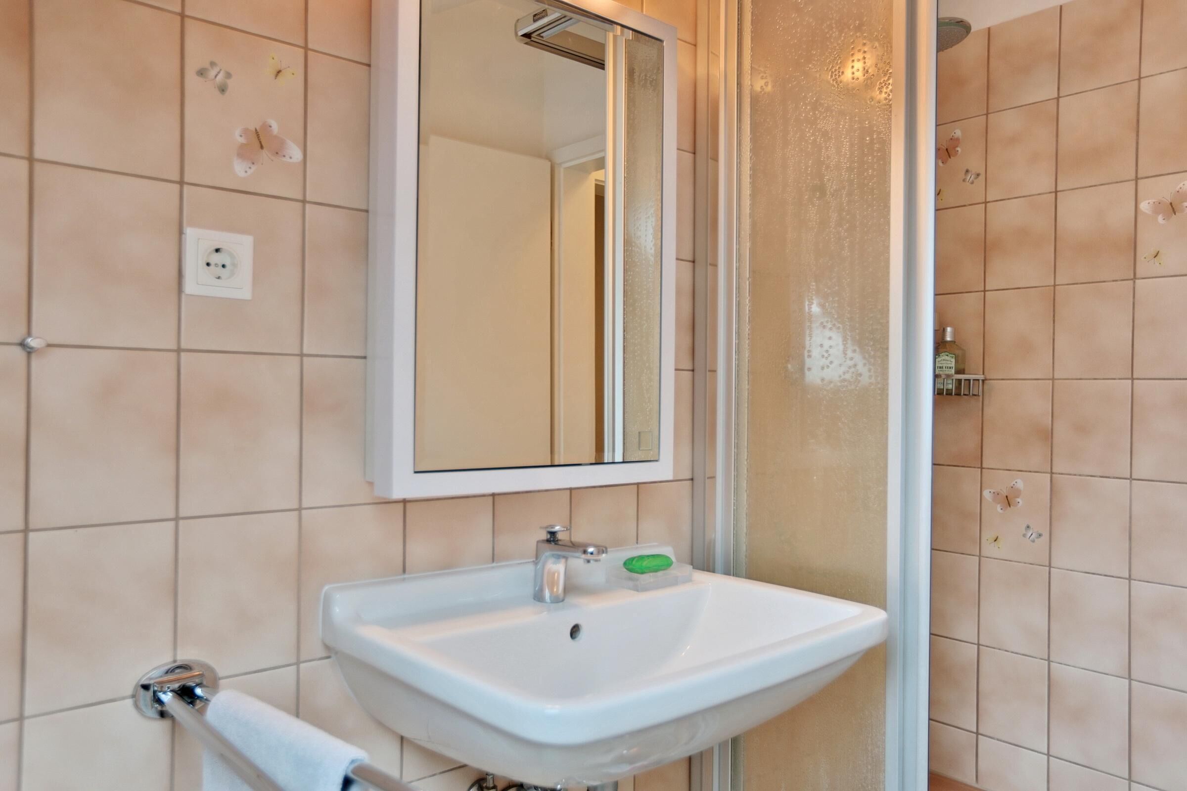 A bathroom with a white sink, a mirror, and a shower area.