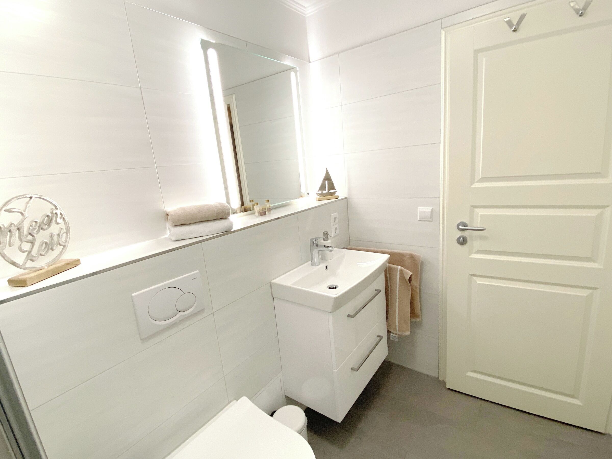 Un baño con azulejos blancos, un lavabo, un espejo y una puerta.