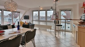 A modern kitchen with large windows, a dining area with a table and chairs, and a kitchen island.