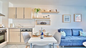 Eine moderne Küche mit weißen Schränken, einem für zwei Personen gedeckten Esstisch und einem blauen Sofa im Wohnbereich.