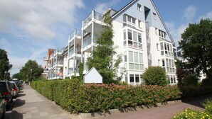 Ein mehrstöckiges Wohngebäude mit Balkonen, einem verschlossenen Eingangsbereich und blauem Himmel.