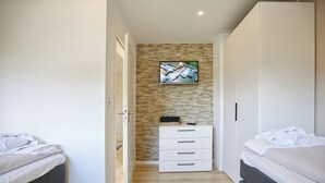 A bedroom with two beds, a white dresser, and a TV mounted on a brick wall. - Ferienhaus Brandt Appartement 3 Möwenkieker (Haffkrug)