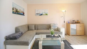 A modern living room with a grey sofa, a glass coffee table, and a wooden cabinet. - Ferienhaus Brandt Appartement 3 Möwenkieker (Haffkrug)
