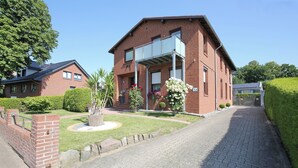 A two-story brick building with a balcony, surrounded by a well-maintained garden and a paved driveway. - Ferienhaus Brandt Appartement 3 Möwenkieker (Haffkrug)