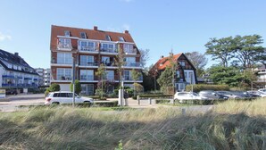 A multi-story residential building with balconies, a parking area with cars, and surrounding greenery. - Windrose Appartement 1 und 3 (Scharbeutz)