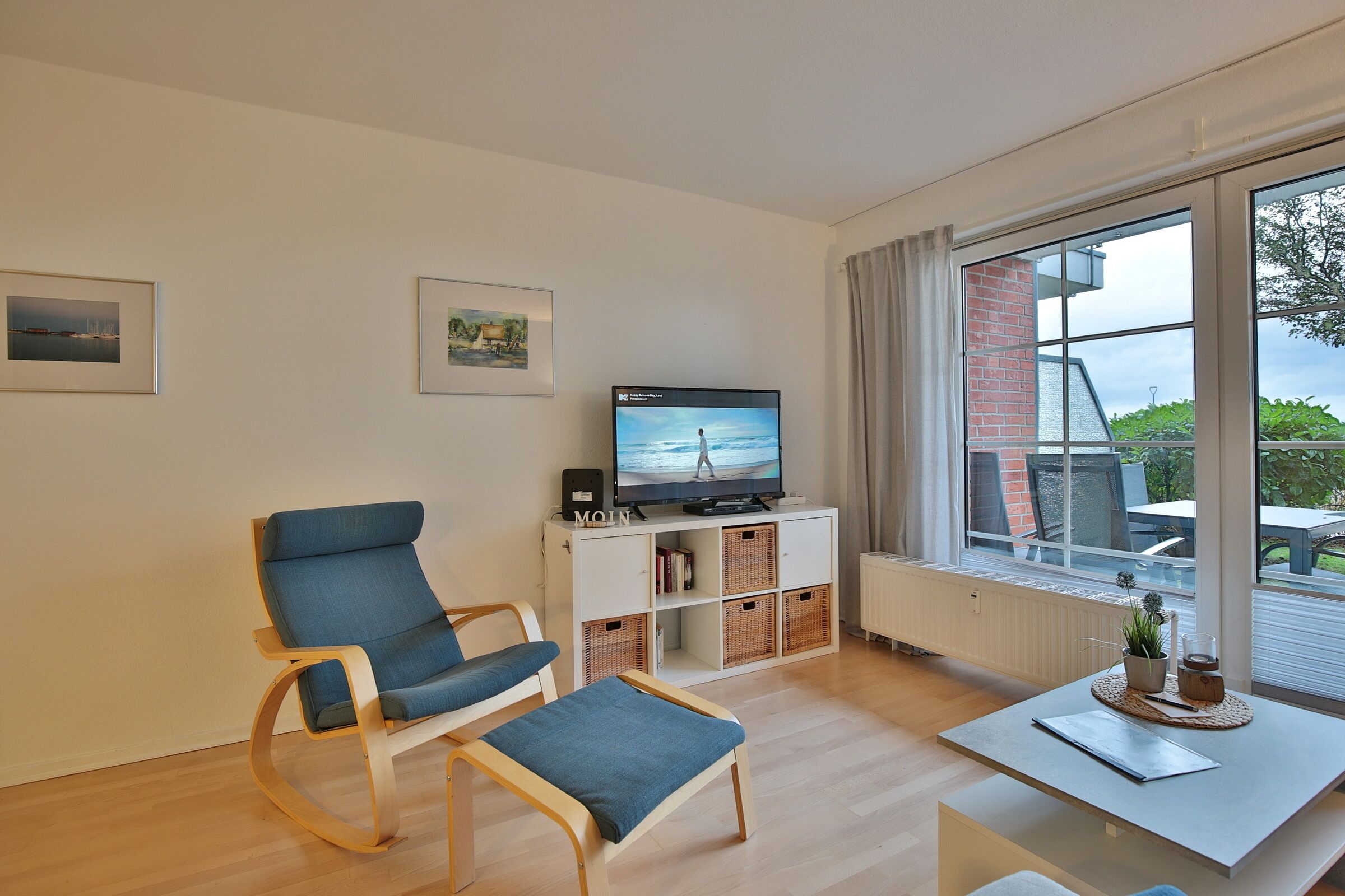 A modern living room with a television, a blue sofa, a small table, and a large window with a view of the outdoors.