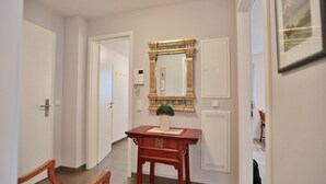 Ein Flur mit einem Holzstuhl, einem kleinen Tisch mit Topfpflanze und einem Spiegel an der Wand.