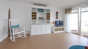 A spacious living room with a white entertainment unit, a rocking chair, and a television. - Meerglück Appartement 5 (Haffkrug)