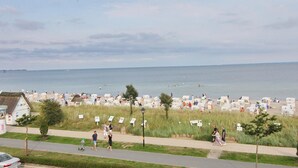 A beachside area with a row of numbered beach huts, a path for pedestrians, and a view of the sea. - Meerglück Appartement 5 (Haffkrug)