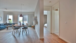 A modern living room with a blue sofa, a dining table with chairs, and a large window with curtains. - Haus Meeresbrise Appartement 18 (Haffkrug)