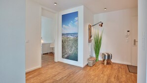 A modern hallway with wooden flooring, a large landscape painting, a standing lamp, and a small table with a plant. - Haus Meeresbrise Appartement 18 (Haffkrug)