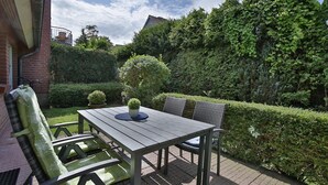Un patio con tavolo e sedie, circondato da siepi curate e un muro in mattoni.