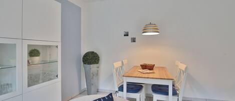 Una cocina moderna con muebles blancos, una mesa de comedor con sillas, una lámpara colgante y una planta en maceta.