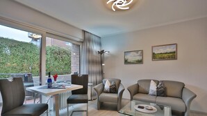 A modern living room with a glass coffee table, leather sofa, and a dining area with a table and chairs. - Haus Hansastrasse Appartement 2 (Scharbeutz)