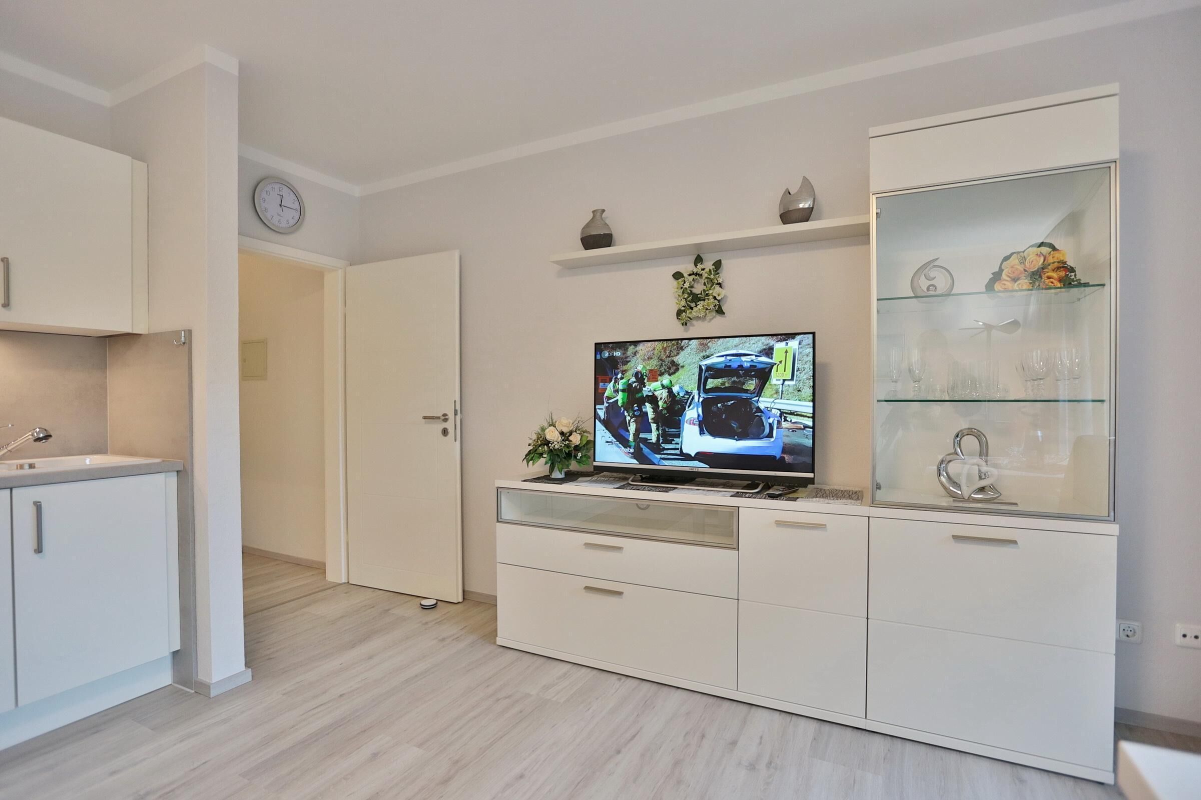 Moderni olohuone, jossa on litteänäyttöinen televisio, valkoiset kaapistot ja lasinen vitriinikaappi.