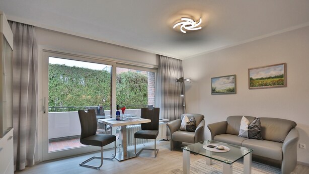 A modern living room with a glass coffee table, a sofa, and a dining area with chairs. - Haus Hansastrasse Appartement 2 (Scharbeutz)