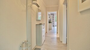 A hallway with a light-colored floor, a door on the left, and a kitchen area visible through an open door at the end. - Haus Hansastrasse Appartement 2 (Scharbeutz)