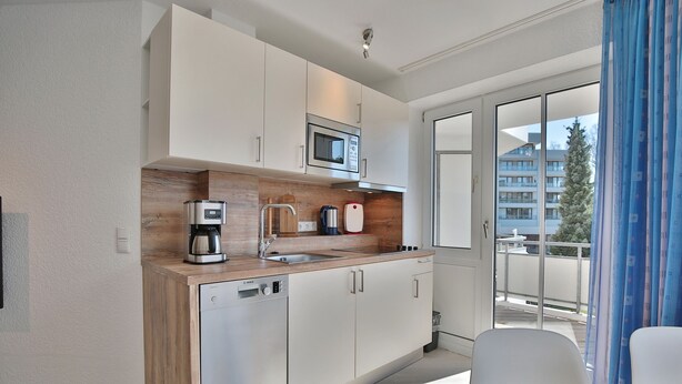 Een moderne keuken met witte kasten, een ingebouwde magnetron en een koffiezetapparaat.