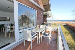 Un patio exterior con una mesa y sillas de vidrio, un muro de ladrillo y vistas a la playa.