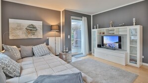 A modern bedroom with a large bed, a TV, and a view of the outdoors. - Ostseeperle Appartement 2 (Scharbeutz)
