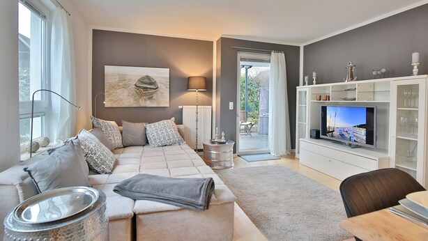 A modern living room with a sofa, TV, and a glass cabinet. - Ostseeperle Appartement 2 (Scharbeutz)