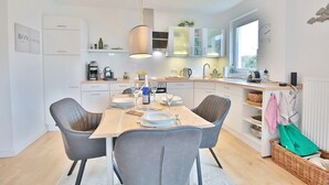 A modern kitchen with white cabinets, a wooden dining table, and two grey chairs. - Ostseeperle Appartement 2 (Scharbeutz)