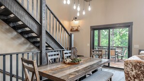 A dining area with a wooden table, benches, and chairs. A staircase with metal railings leads to an upper level. - New Spacious 3200 sq. ft. Cabin w/ Hot Tub Across Street from Clubhouse Pool (Lead)