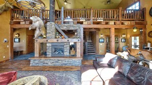 A spacious living area with a stone fireplace, a high wooden ceiling, and a leather sofa. - New Spacious 3200 sq. ft. Cabin w/ Hot Tub Across Street from Clubhouse Pool (Lead)