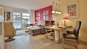 A modern living room with a dining area, a sofa, a chair, and a table with a lamp. - Strandperle Appartement 203 (Haffkrug)