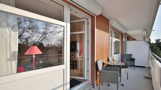 A balcony with a table and chairs, a red lamp, and a view of the interior through a glass door. - Strandperle Appartement 203 (Haffkrug)