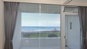 Ein Zimmer mit einem großen Fenster, das mit Jalousien verdeckt ist, Meerblick und einer Tür mit Griff.
