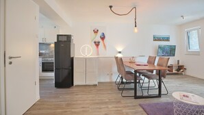 Een moderne keuken met een zwarte koelkast, een magnetron en een oven. Er is een eethoek met een houten tafel en stoelen.