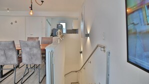 Een moderne woonkamer met een eethoek, een trap en een tv waarop een sportzender wordt vertoond.