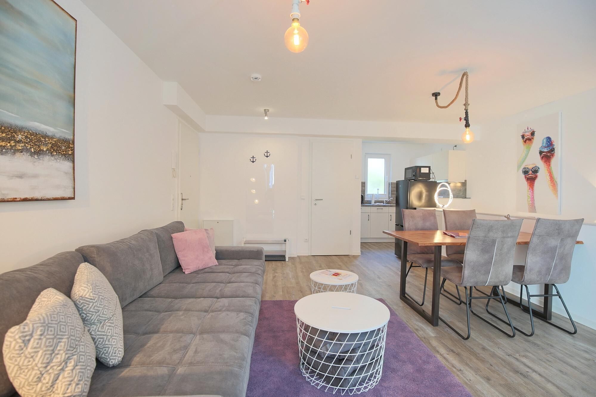 Un salon moderne avec un canapé gris, une table basse et un coin repas comprenant une table et des chaises en bois.