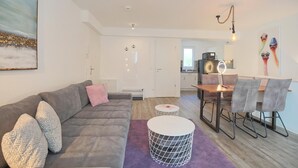 Een moderne woonkamer met een grijze bank, een salontafel, en een eethoek met een houten tafel en stoelen.