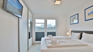 Ein Hotelzimmer mit einem großen Bett, einem an der Wand befestigten Fernseher und einem Fenster mit Blick auf Bäume und Gebäude.