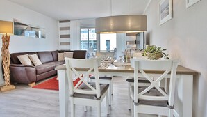Uma sala de estar moderna com um sofá de couro marrom, cadeiras brancas, uma mesa de jantar e uma luminária pendente grande.