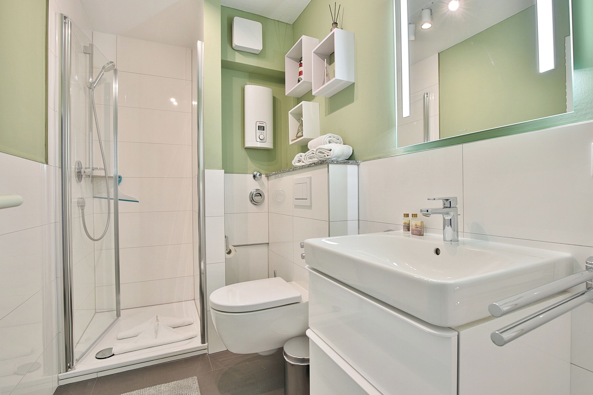 A modern bathroom with a glass-enclosed shower, a white toilet, and a large sink with a mirror above.