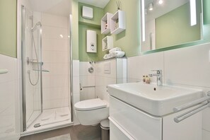 Een moderne badkamer met een douchecabine van glas, een wit toilet en een grote wastafel met een spiegel erboven.
