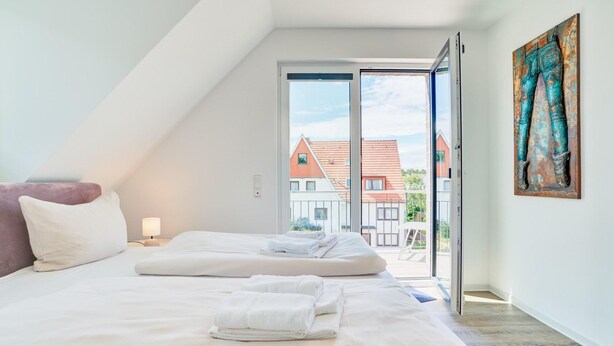 Ett sovrum med två sängar, en tavla och utsikt över hus genom en öppen dörr.