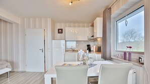 Een moderne keuken met witte kasten, een eettafel met stoelen en een raam met uitzicht op bomen.