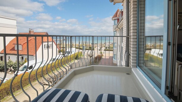 A balcony with two striped lounge chairs, a clear view of the neighborhood, and a building with a red roof in the background. - Strandschlösschen Appartement 28 (Haffkrug)