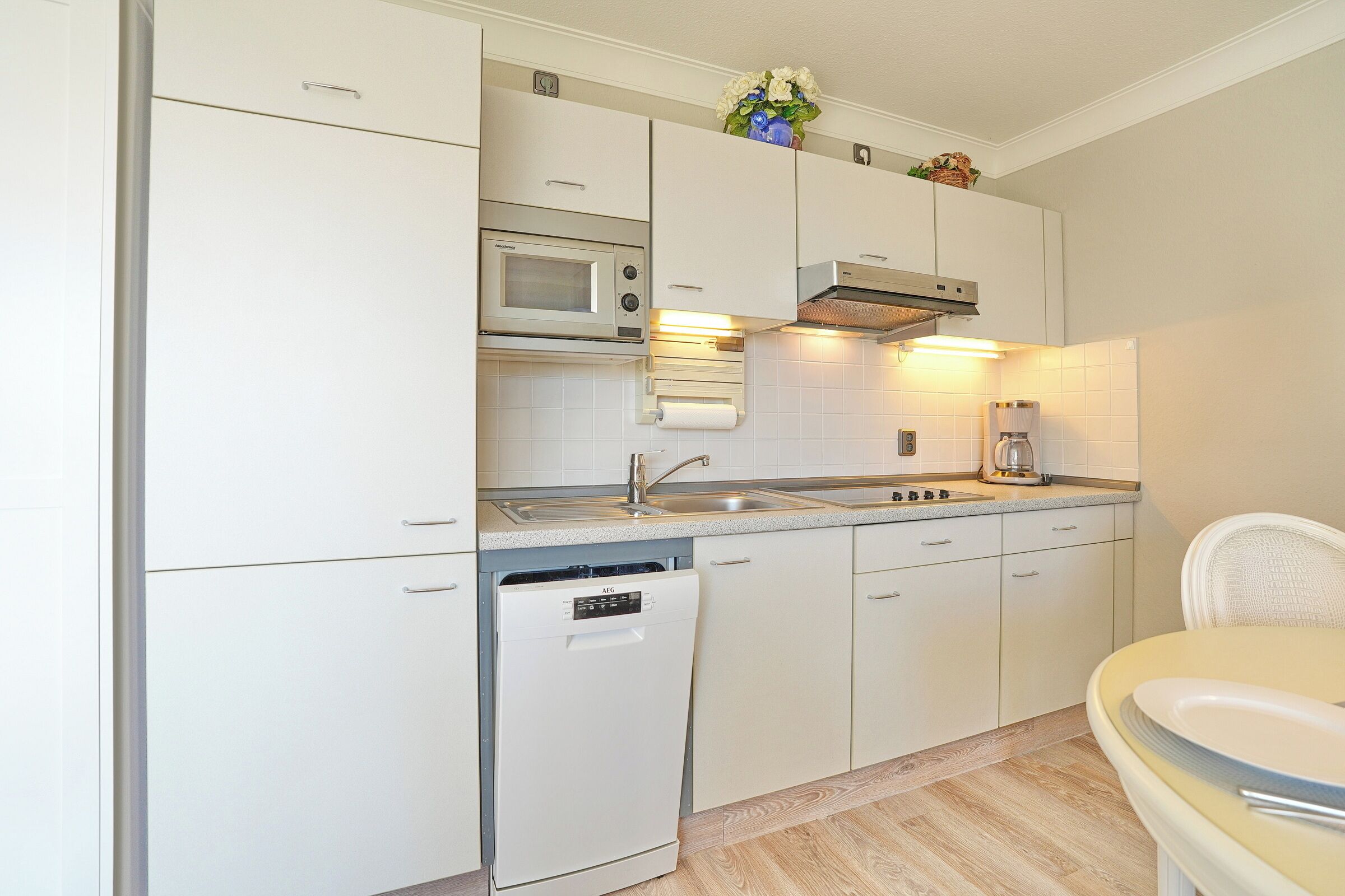 A compact kitchen with white cabinetry, a built-in microwave, a dishwasher, and a coffee maker.