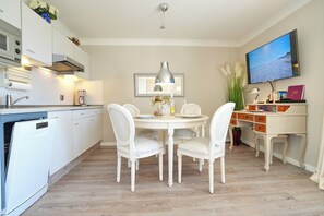 Cozinha moderna com armários brancos, uma mesa de jantar com cadeiras, uma TV fixada na parede e um vaso com planta.