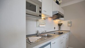 A modern kitchen with white cabinetry, stainless steel appliances, and a double sink. - Strandschlösschen Appartement 28 (Haffkrug)