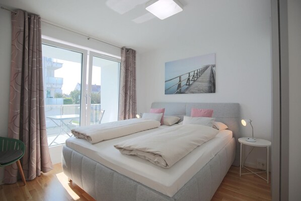 Une chambre moderne avec un grand lit, une petite table de chevet et une vue sur l’extérieur grâce à une porte-fenêtre coulissante.