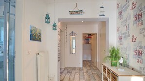 Ein Flur mit Holzboden, Heizkörper, Glastür, einem Gemälde und einer Wand mit nautisch gestalteter Tapete.