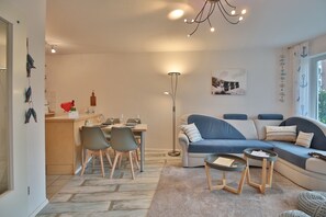 En moderne stue med en blå sofa, et spiseområde med bord og stole, og et køkken med en køkkenø og hårde hvidevarer.