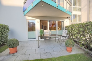 En terrasse med et bord og stole, plantekasser og udsigt til bygningens indre.